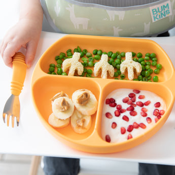 Close-up of a child eating yogurt, fruit, & veggies from an orange divided plate with Bumkins Spoon + Fork: Tangerine.