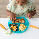 A child enjoys fruit, macaroni, pizza, and yogurt from a Bumkins Silicone Grip Dish: Blue Jelly on a white table.