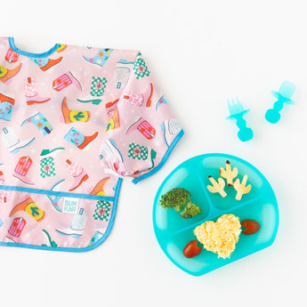 Bumkins Silicone Grip Dish: Blue Jelly with veggies lays on a white background with matching utensils and a pink cowboy boot patterned bib.