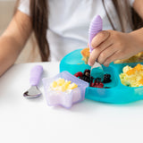 A child enjoys breakfast from a Bumkins Silicone Grip Dish: Blue Jelly, using a lavender fork, with yogurt and pineapple in a star bowl.