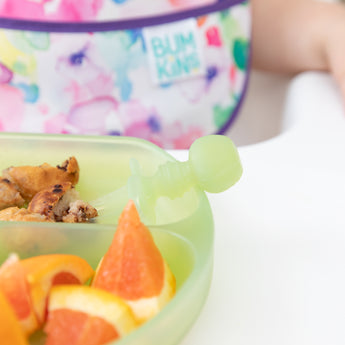 Close-up of a Bumkins Silicone Chewtensils®: Green Jelly sitting in a green plate with pancake and orange pieces.