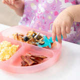 Close-up of a child eating waffles and berries with a blue fork from a Bumkins Silicone Grip Dish: Pink Jelly at a white table.