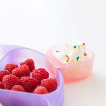 Close-up of Bumkins Silicone Grip Dish: Purple Jelly with raspberries and a pink heart-shaped cup of whipped cream on a white background.