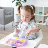 A toddler with pigtails sits in a high chair, enjoying scrambled eggs and fruit from a Bumkins Silicone Grip Dish: Purple Jelly.