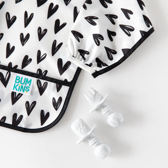 Close-up of Bumkins Silicone Chewtensils®: Marble next to a black & white heart-patterned sleeved bib on a white background.