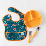 A Bumkins SuperBib® 3 Pack: All Together Now lays flat on a white background next to an orange divided plate and orange utensils.