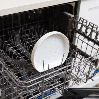 Bumkins Silicone Grip Plate: Vanilla Sprinkle sits in the top rack of an open dishwasher.