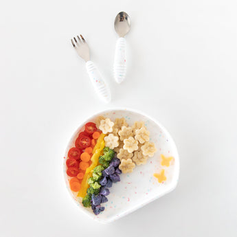 Rainbow-colored food on a Bumkins Silicone Grip Plate: Vanilla Sprinkle, with a fork and spoon above on a white background.
