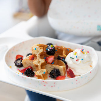 Bumkins Silicone Grip Plate: Vanilla Sprinkle holds a waffle topped with berries, whipped cream, and sprinkles on a high chair tray.