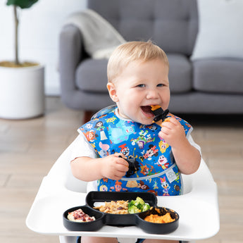 A baby in a high chair uses a silicone feeding set from the Growing with Bumkins Gift Set, Disney Mickey Mouse by Bumkins.