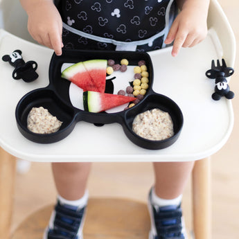 A child enjoys watermelon, cereal balls, and oatmeal on a Mickey plate using the Growing with Bumkins Gift Set, Disneys Mickey Mouse.