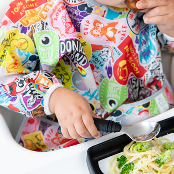 Child in a colorful outfit eating spaghetti from the Bumkins Growing with Bumkins Gift Set, Disney Mickey Mouse plate.