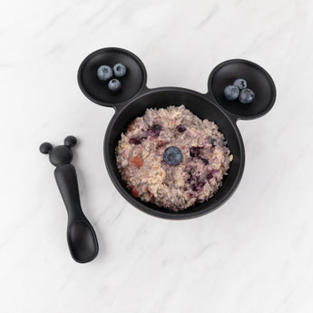 Bowl of oatmeal with blueberries in a Growing with Bumkins Gift Set, Disney Mickey Mouse (by Bumkins), on a white marble surface.