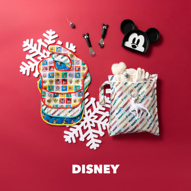 Disney baby items on a red background: bibs, Mickey Mouse plate, utensils, snowflakes, and a holiday-themed gift bag.