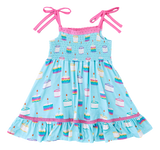Harlow Smocked Birdie Dress by Birdie Bean in blue with pink straps and cake patterns, made from comfy bamboo viscose.