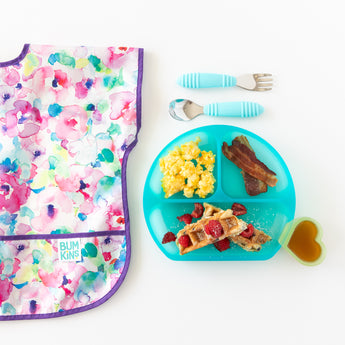 A bib, blue plate with breakfast foods, and utensils beside a Bumkins Silicone Little Dipper Combo 2 Pack: Aqua Jelly on a white background.
