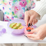 Hands attach a Bumkins Silicone Little Dipper Combo 2 Pack: Magenta Jelly filled with tomatoes to a purple bowl of food on a high chair tray.