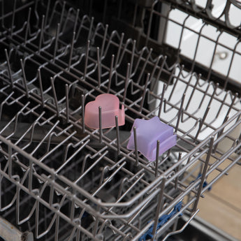 Two dipping cups from Bumkins Grip Dish Deluxe Infant 5-Piece Mealtime Set: Pink Jelly sit in the top rack of an open dishwasher.