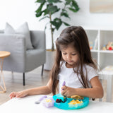 A young girl at a table enjoys fruit and eggs with a fork from a plate with a Bumkins Silicone Little Dipper Combo 2 Pack: Magenta Jelly.