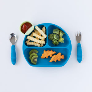 Bumkins Silicone Grip Dish: Dark Blue holds dinosaur nuggets, fries, fruit, & veggies on a white background next to matching utensils.