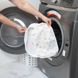 A person holds a bag from Bumkins The Outfit Organizer Essential 5-Piece Set: Palm Daze in front of an open front-loading washing machine.