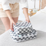 A person stacks Bumkins Packing Cube 2 Pack + Clear Travel Bag 3 Pack Set in Charcoal Check for smart travel organization.