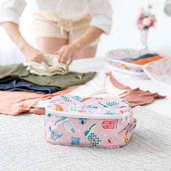 The Bumkins Packing Cube 2 Pack + Clear Travel Bag 3 Pack Set: Boots, in pastel prints, sits on a bed as clothes are folded.