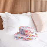 Two bags from Bumkins The Outfit Organizer Essential 5-Piece Set: Boots sit stacked on a white bed with a wood headboard & white pillows.