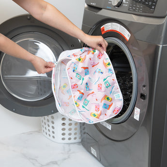 A person holds a Bumkins Packing Cube 2 Pack: Boots in front of an open front-loading washing machine.