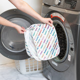 A person holds a Bumkins Packing Cube 2 Pack: Mickey & Friends Varsity in front of an open front-loading washing machine.