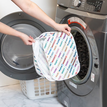 A person holds a bag from Bumkins The Outfit Organizer Essential 5-Piece Set: Mickey & Friends Varsity in front of an open washing machine.