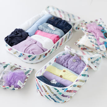 Close-up of Bumkins The Outfit Organizer Essential 5-Piece Set: Mickey & Friends Varsity with clothes and toiletries on a white background.