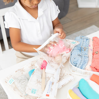 A child packs toiletries into a bag from Bumkins The Outfit Organizer Essential 5-Piece Set: Palm Daze on a white table.