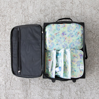 Open suitcase on gray carpet, neatly packed with Bumkins Aloha Stitch packing cubes and clear travel bags for toiletries.