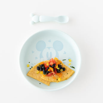Bumkins Silicone Plate + Spoon Set: Disney Mickey Mouse holds a quesadilla, black beans, tomatoes, and peppers on a white background.