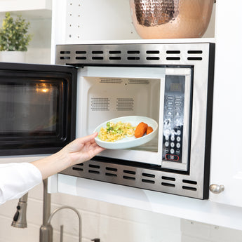 A person places Bumkins Silicone Plate + Spoon Set: Disney Mickey Mouse filled with pasta and veggies into an open microwave.