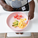 A toddler wearing a bib enjoys breakfast from Bumkins Silicone Plate + Spoon Set: Disney Minnie Mouse in their high chair.