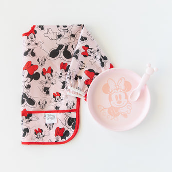 Bumkins Silicone Plate + Spoon Set: Disney Minnie Mouse sits next to a bib featuring Minnie Mouse illustrations on a white background.