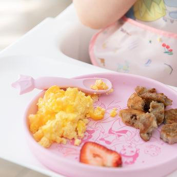 Bumkins Silicone Plate + Spoon Set: Disney Princess with eggs, sausage, a strawberry slice on a high chair tray.