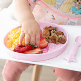 A child's hand reaches for food from Bumkins Silicone Plate + Spoon Set: Disney Princess with eggs, sausage, and strawberries on a high chair.
