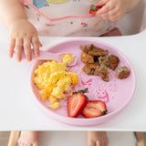 A child in a high chair enjoys breakfast from Bumkins Silicone Plate + Spoon Set: Disney Princess while wearing a pink bib.