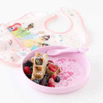 Bumkins Silicone Plate + Spoon Set: Disney Princess holding a waffle, berries, and powdered sugar sits next to a bib on a white background.