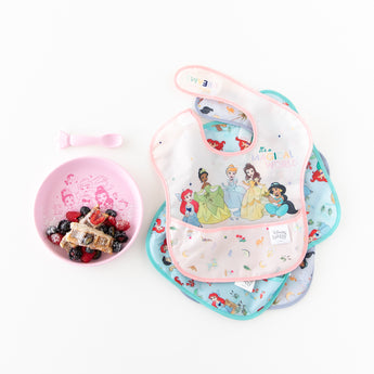 Bumkins Silicone Plate + Spoon Set: Disney Princess with berries and waffles on a white background next to waterproof bibs.
