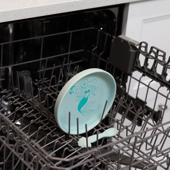 Bumkins Silicone Plate + Spoon Set: Disney Princess Ariel sits in the top rack of an open dishwasher.