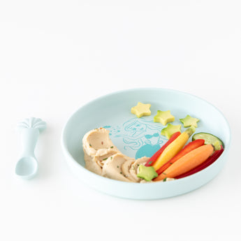 Bumkins Silicone Plate + Spoon Set: Disney Princess Ariel filled with hummus, cucumber, and baby carrots on a white background.