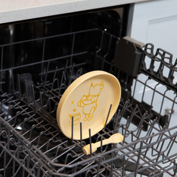 Bumkins Silicone Plate + Spoon Set: Disney Winnie the Pooh sits in the top rack of an open dishwasher.