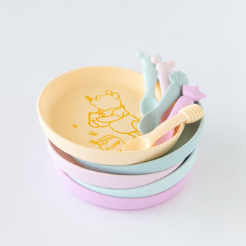 Bumkins Silicone Plate + Spoon Set: Disney Winnie the Pooh is stacked on top of other similar plates on a white background.