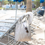 A bag from Bumkins The Playdate Planner Deluxe 5-Piece Set: Lunar Phase with sunglasses, water bottle, and towel hangs off a lounge chair.