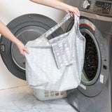 A person holds a bag from Bumkins The Playdate Planner Deluxe 5-Piece Set: Lunar Phase in front of an open front-loading washing machine.