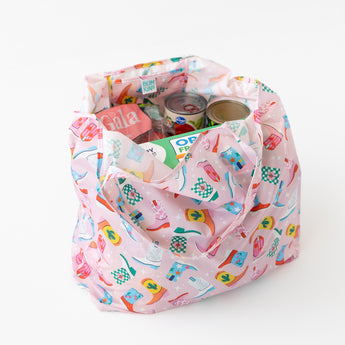 A bag from Bumkins The Playdate Planner Deluxe 5-Piece Set: Boots sits on a white background with groceries and canned goods inside.